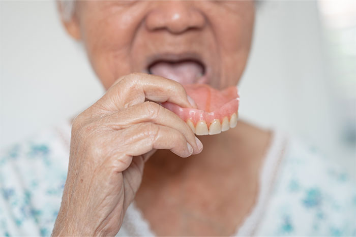 Elderly person holding dentures near mouth, illustrating moments of realizing they were doing something the wrong way.