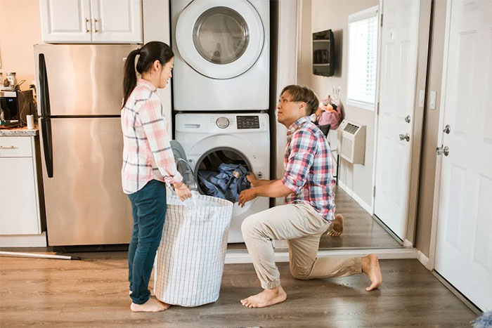Couple in laundry room, man kneeling by washing machine, illustrating common mistakes.