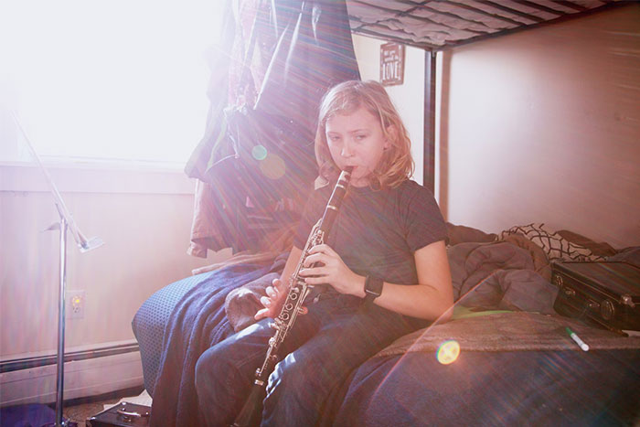 Young girl sitting on bed playing clarinet with sunlight streaming through window, realizing she was doing something wrong