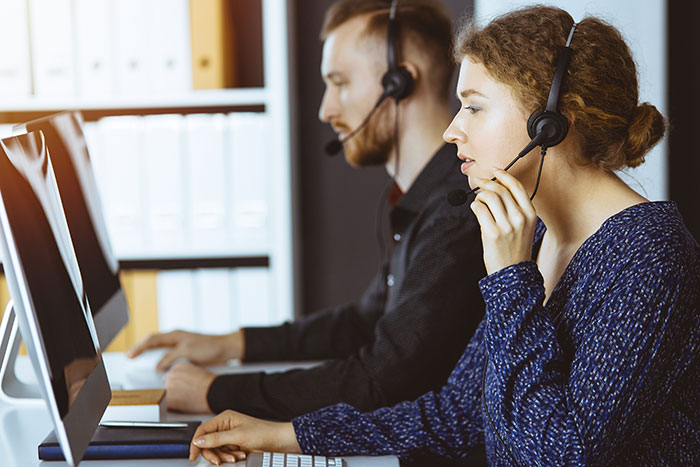 Two call center employees working at computers with headsets, representing job quit scenarios.