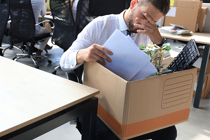 Man leaving office on first day, carrying a box of belongings, looking stressed and overwhelmed.