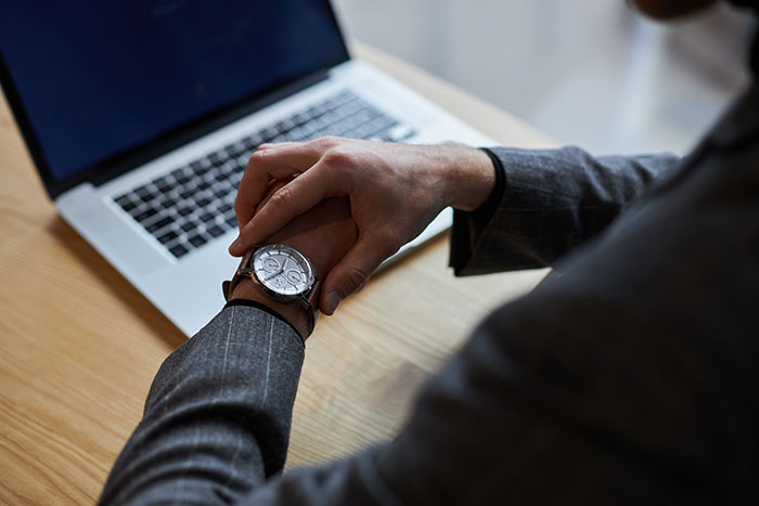 Person in a suit checking watch near a laptop, symbolizing quitting jobs on the first day.