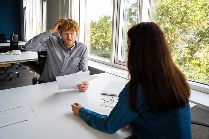 A man looks confused while holding papers during a meeting; represents quitting jobs on the first day.