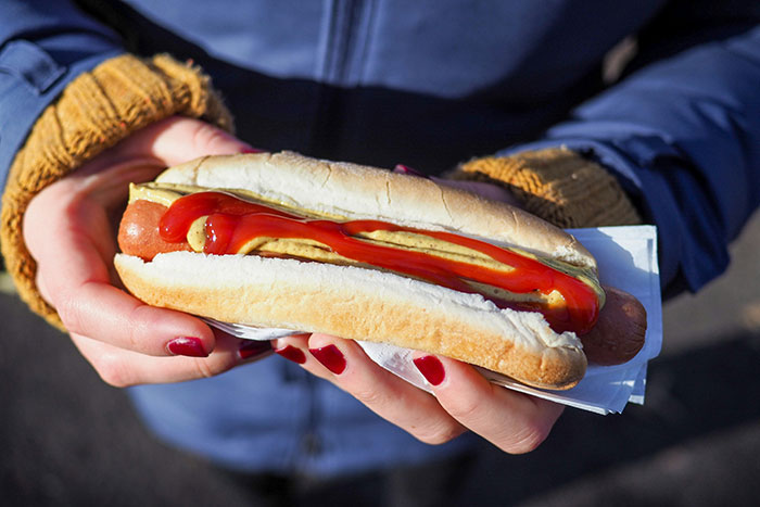 Person holding a hot dog with mustard and ketchup, representing experiences of quitting jobs on the first day.