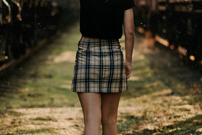 Person in a plaid skirt walking along a grassy path between train tracks, symbolizing quitting a job.