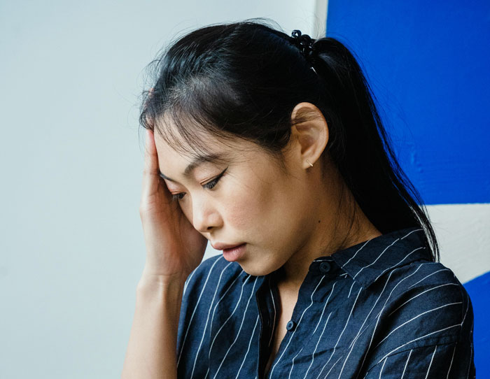 29YO woman looking stressed, in a striped shirt, pondering family expectations, related to babysitting nephews.