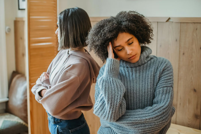 Two women standing back-to-back in a room, one looking frustrated; concept of freedom and family expectations.