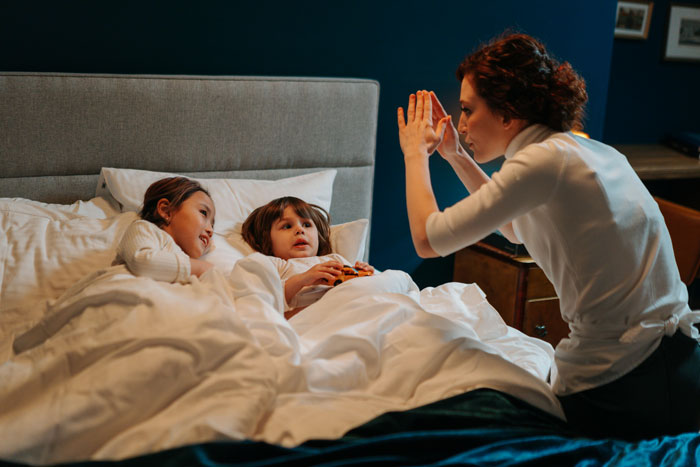A woman entertains two children in bed, engaging in storytelling.