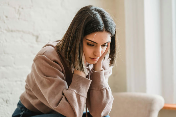 Distraught restaurant worker sitting alone, wearing a brown sweater, contemplating an unexpected work situation.