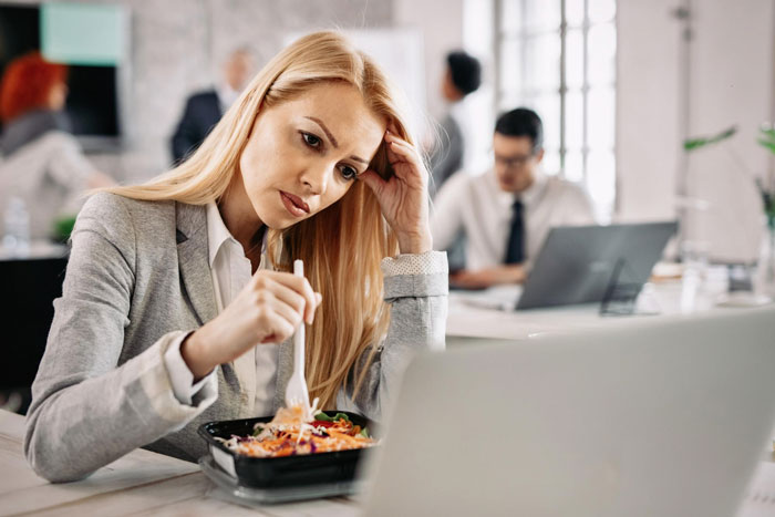 Woman eating lunch alone at work desk, illustrating team spirit conflict.