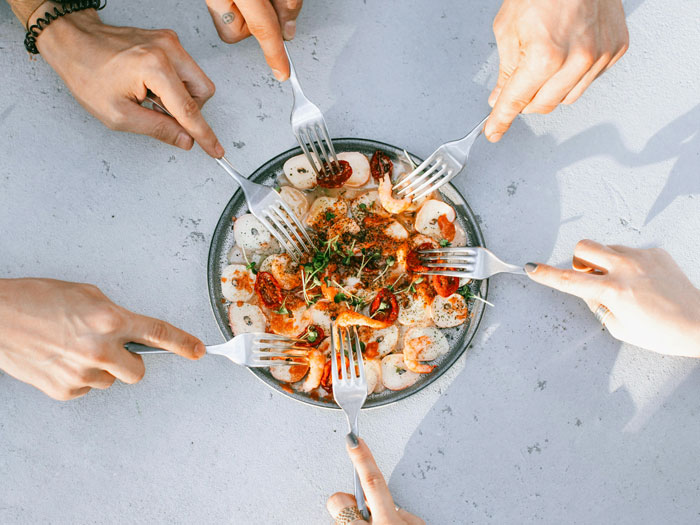 Hands with forks reaching for a shared dish, symbolizing team spirit and food sharing at work.