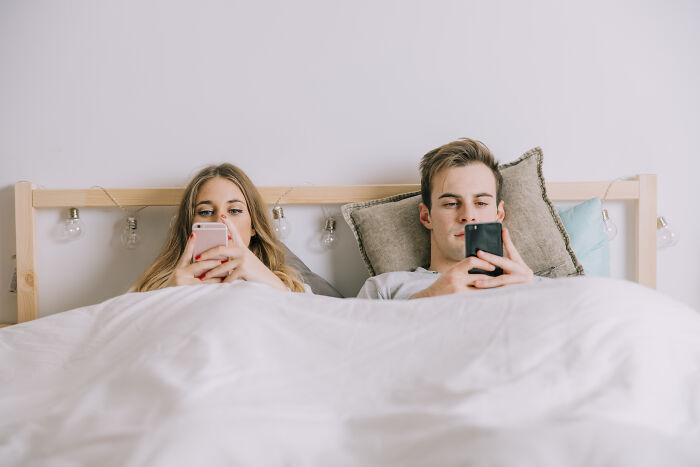 A couple in bed looking at their phones, highlighting regret and disconnect in marriage with a spouse.