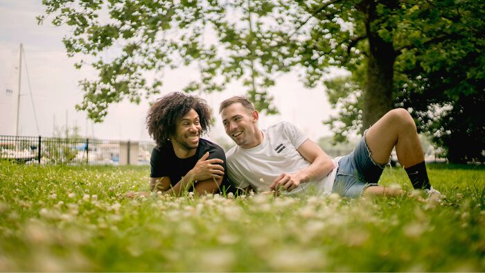 Two friends relaxing on grass, smiling and sharing stories, enjoying a sunny day outdoors.