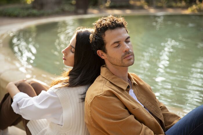 Couple sitting back to back by a pond, reflecting emotions related to regret-marriage-spouse.