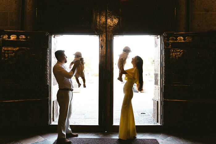 A couple standing in doorways, each holding a child, highlighting marriage and family dynamics.