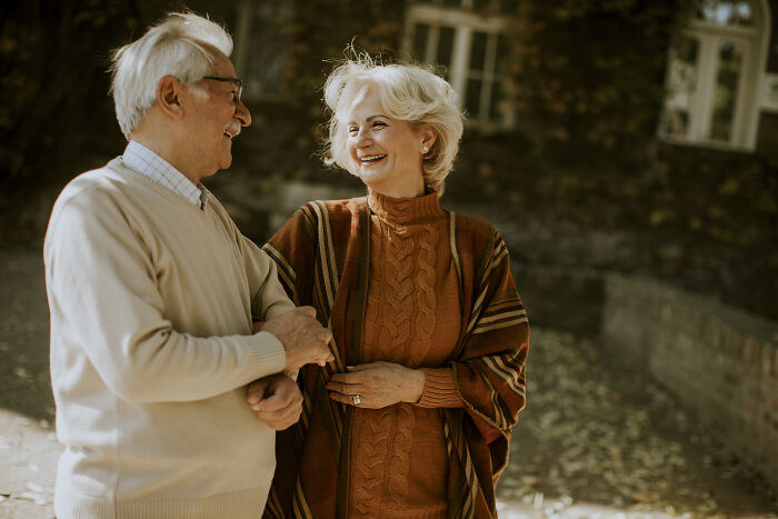 Elderly couple smiling and holding hands outdoors, showcasing respect in a parents' relationship of decades.