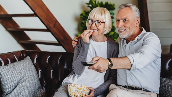 Elderly couple enjoying popcorn on a sofa, showcasing the respect and bond in parent relationships over decades.