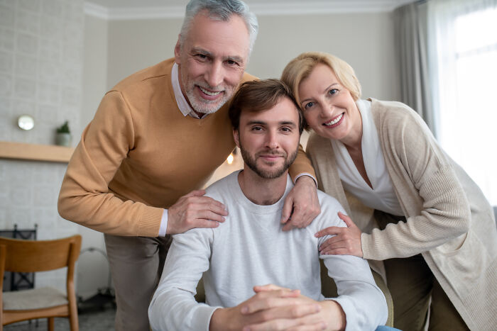 Smiling parents standing close to an adult son in a cozy living room, illustrating respect in a multi-decade relationship.