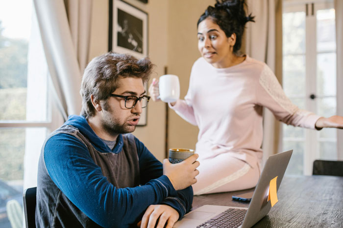 Man with glasses at laptop, woman in loungewear holding mug, discussing returning shoes. Man with glasses at laptop, woman in loungewear holding mug, discussing returning shoes.