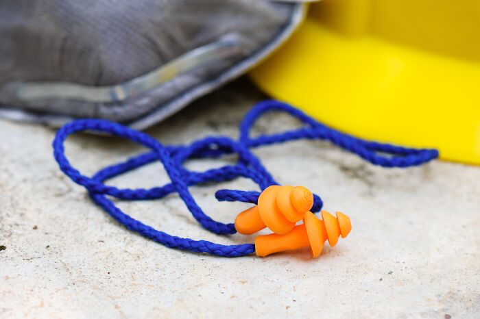 Orange earplugs with a blue cord on a concrete surface, travel essentials for a more peaceful journey.