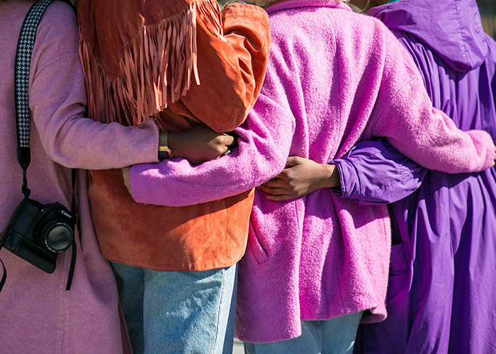 Women linked arm in arm, wearing colorful jackets, representing proactive measures and unity.