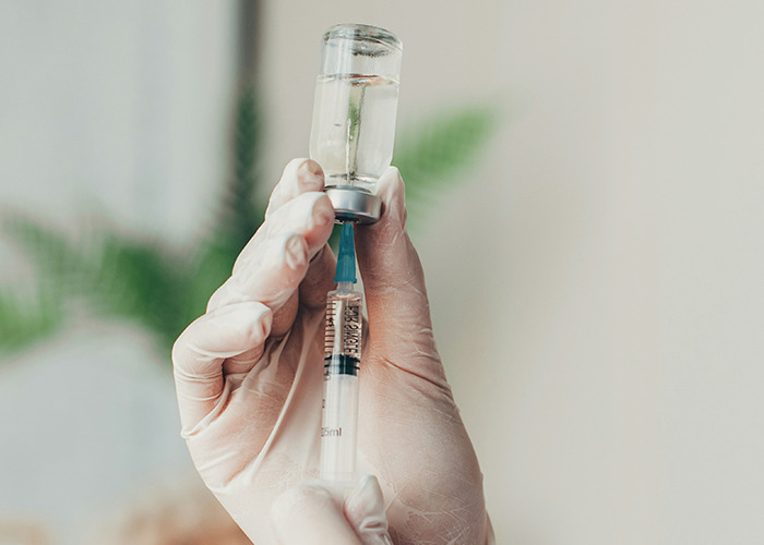 A gloved hand prepares a vaccine syringe, a proactive health measure.