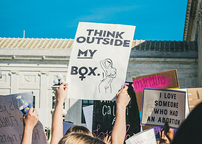 Women holding protest signs advocating for proactive health measures, including empowering statements for women's rights.
