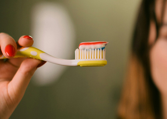 Hand holding a toothbrush with toothpaste; discussing proactive health measures.