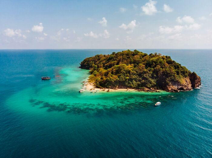 Aerial view of a secluded island, often associated with rich people's exclusive escapes, surrounded by clear turquoise waters.