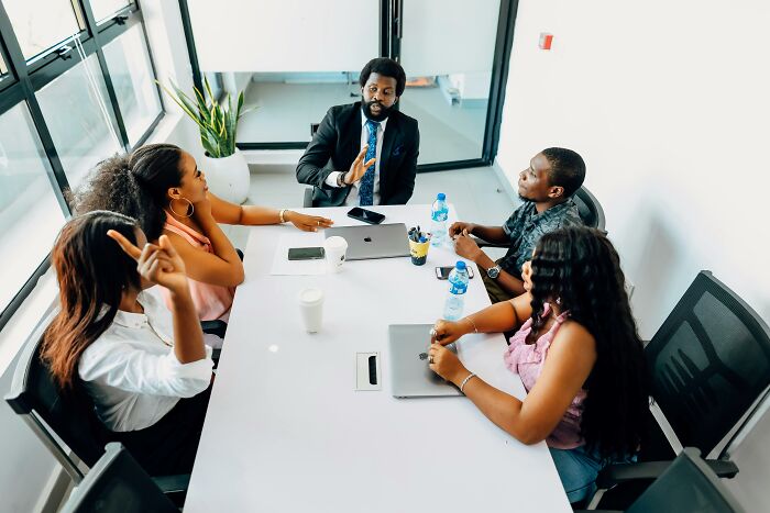 Five people in a meeting room, some appear frustrated, possibly discussing rich people's behavior.