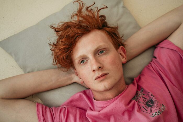Person in a pink shirt lying on a cushion with arms behind head, contemplating how annoying rich people can be.