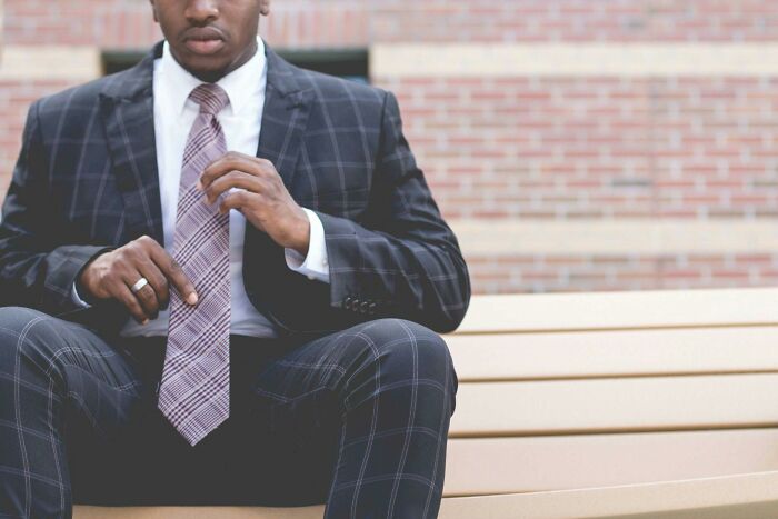 Man sitting on bench in suit adjusting tie