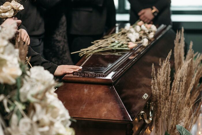 Hands touch a polished coffin surrounded by flowers, symbolizing the unexpected path to wealth.