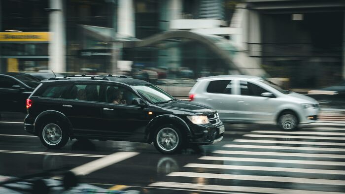 Two cars crossing a busy city intersection in the rain, illustrating stories of overnight wealth.