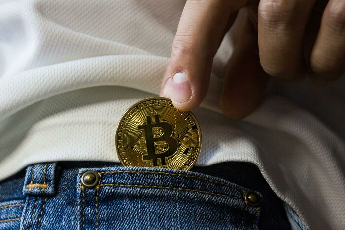 A hand placing a Bitcoin coin into the pocket of blue jeans, symbolizing overnight wealth.