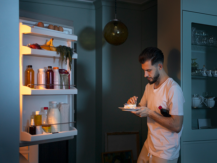 Man in kitchen eating by open fridge at night, linked to mozzarella theft incident. Man in kitchen eating by open fridge at night, linked to mozzarella theft incident.