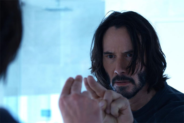 Person with shoulder-length hair making a gesture, focusing intently in a reflective space.