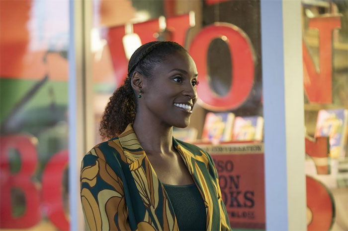 A woman smiling in a colorful jacket, standing outside a bookshop, under evening lights.