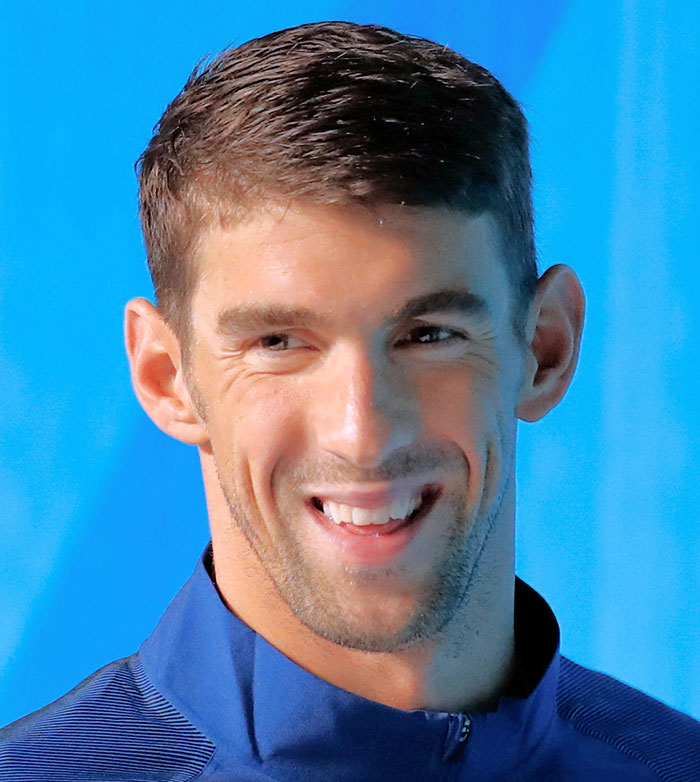 Smiling celebrity in a blue jacket against a blue background.