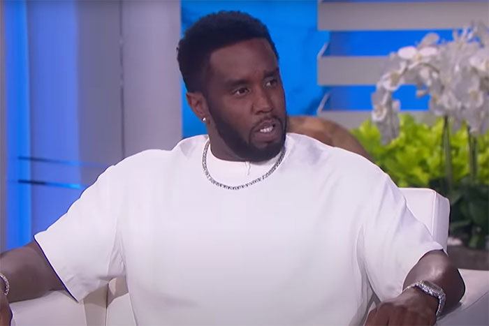 Celebrity in a white shirt sitting on a talk show set, discussing an incident or story.