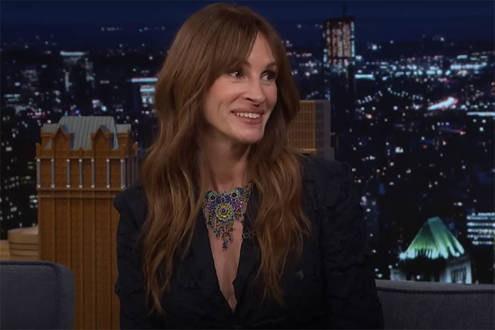 Smiling woman in a cityscape night setting, wearing a colorful necklace.