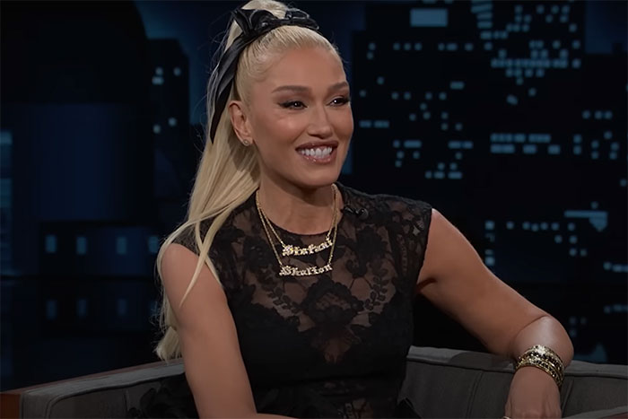 A person in a black lace top on a TV show set, smiling, with a cityscape backdrop, discussing celebrity encounters.