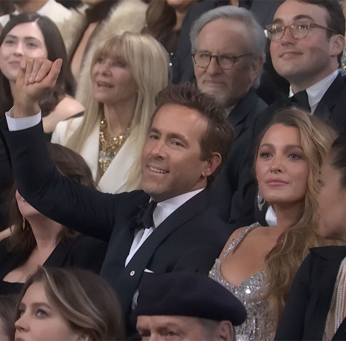 Audience at a live event, with a man raising his hand and others seated around, capturing a candid moment. Audience at a live event, with a man raising his hand and others seated around, capturing a candid moment.