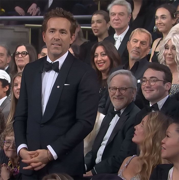 Celebrity in a tuxedo standing among a seated audience at a formal event. Celebrity in a tuxedo standing among a seated audience at a formal event.