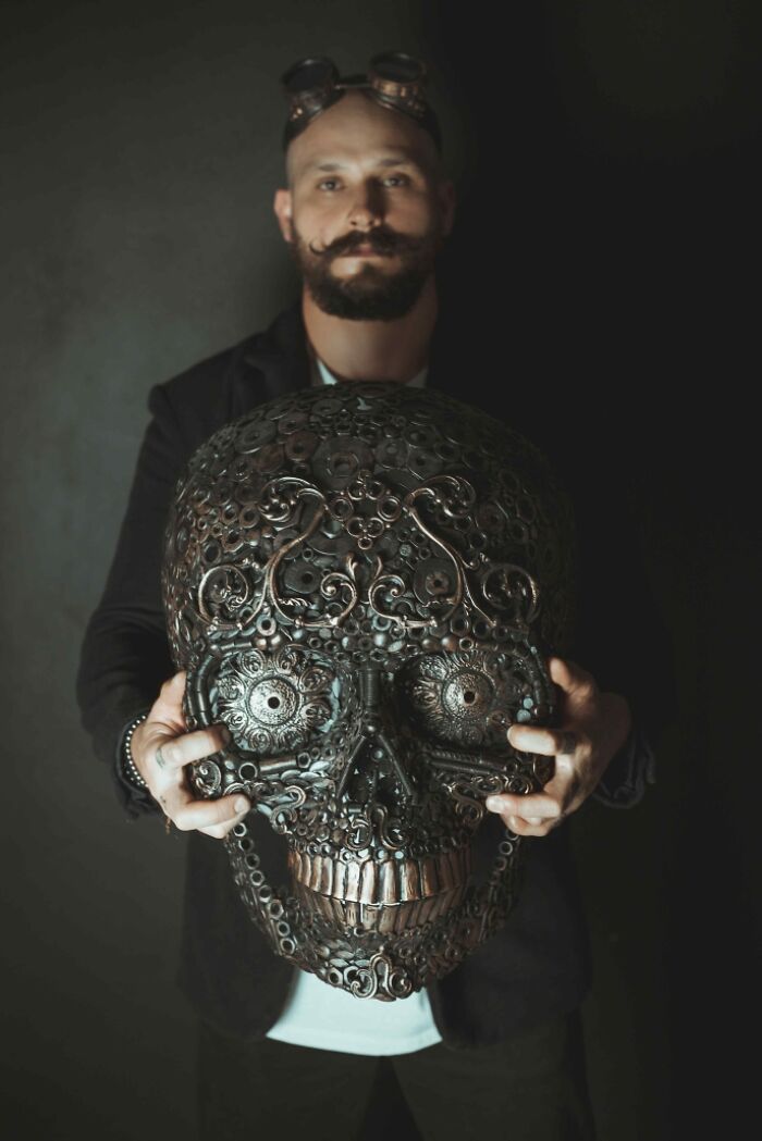 Artist holding a skull sculpture made from scrap metal, demonstrating incredible craftsmanship and creativity.
