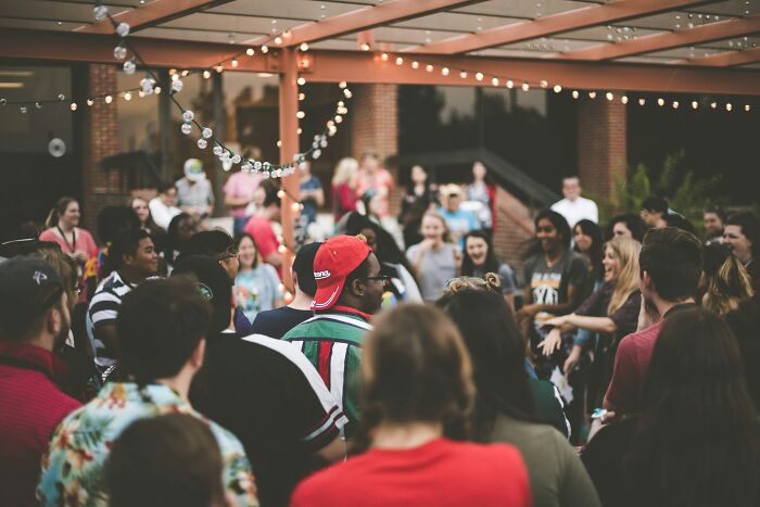 A crowd of people socializing outdoors under string lights.