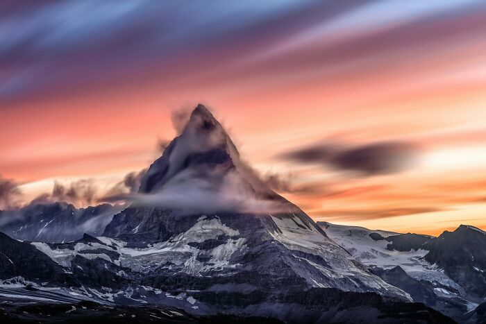 Mountain peak at sunset showcasing natural wonders with vibrant skies and clouds.