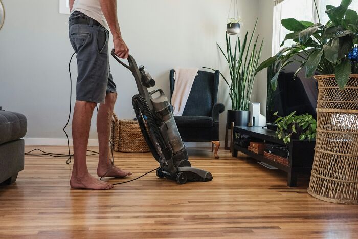 Person vacuuming a hardwood floor in a living room, showcasing a durable and beautifully designed vacuum cleaner.