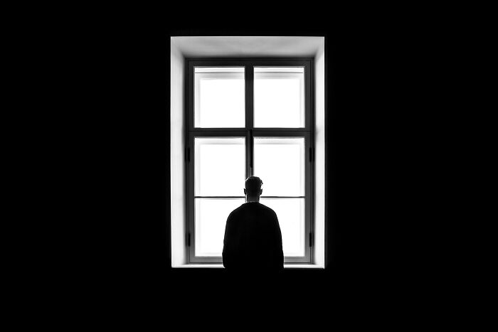 Silhouette of a person standing alone at a window, symbolizing the solitude faced in adulthood challenges.