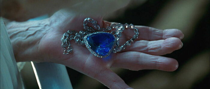 Old hand holding a famous movie prop, a heart-shaped blue diamond necklace.